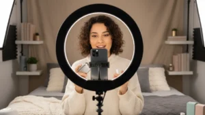Content creator filming product review with smartphone on tripod and ring light in bedroom studio setup, representing content creation as side hustle